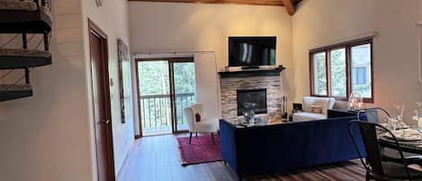 Un vaste espace de vie doté d’un plafond en bois, d’une cheminée, d’un téléviseur et d’un coin repas avec une table et des chaises.