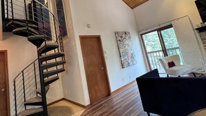 Un vaste espace de vie doté d’un plafond en bois, d’un escalier en colimaçon, d’une grande fenêtre et d’un canapé moderne.