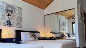 Une chambre moderne avec deux lits, un plafond en bois et des œuvres d’art accrochées au mur.