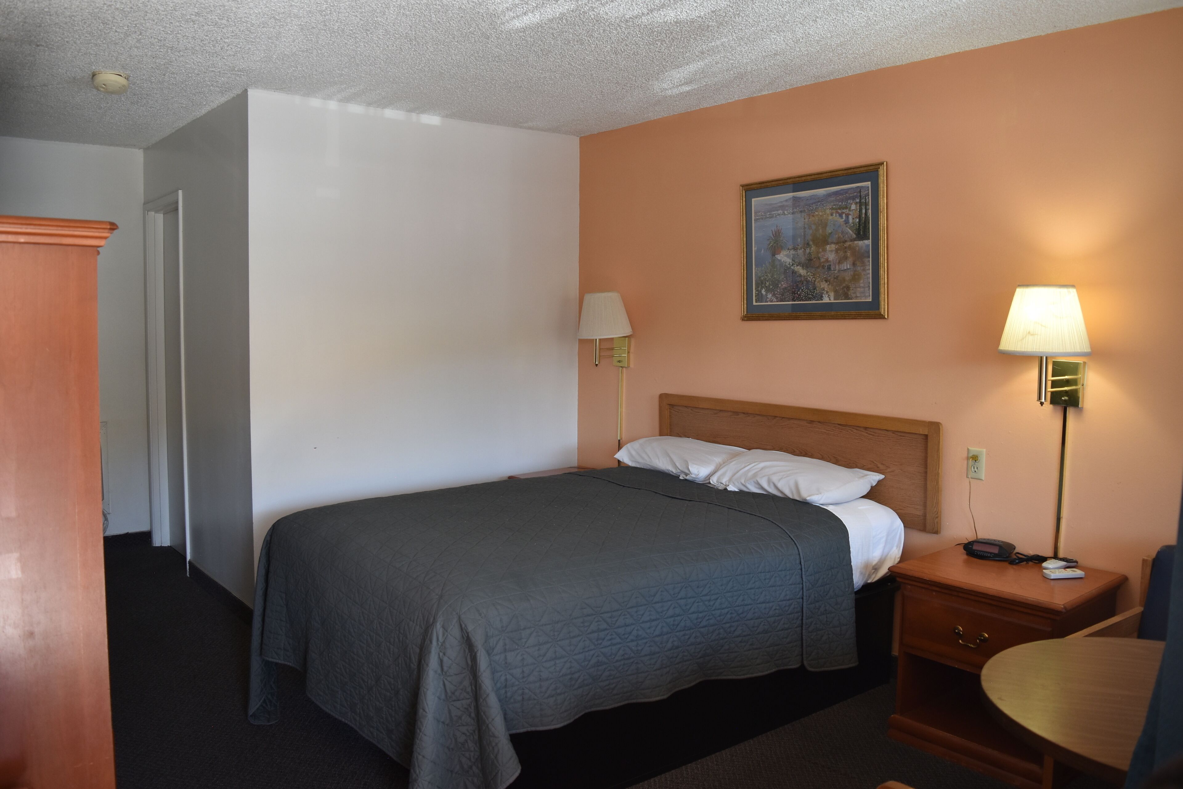 Habitación de hotel con cama, lámparas de noche, un cuadro en la pared y una mesita de noche de madera.