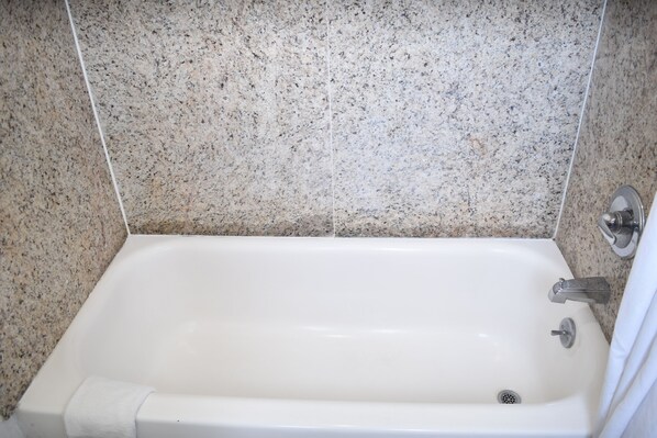 A white bathtub with a chrome faucet and a drain, set against a speckled tile wall. - Arlington inn (Arlington)