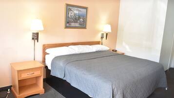 A hotel room with a bed, two bedside lamps, a nightstand with a drawer, a framed picture on the wall, and a window with a white curtain.