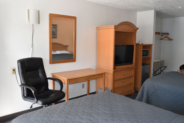 A hotel room with a bed, a desk with a chair, a television, a wardrobe, and a mirror. - Arlington inn (Arlington)