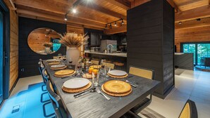 A modern dining area with a long wooden table set for six, surrounded by dark wooden walls and a large mirror.