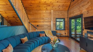 A modern log cabin interior with a large blue sectional sofa, a small round table with a vase, and a TV on a cabinet.