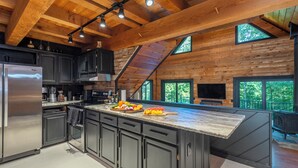 A modern kitchen with dark cabinets, a stainless steel refrigerator, and a large island with a marble countertop.