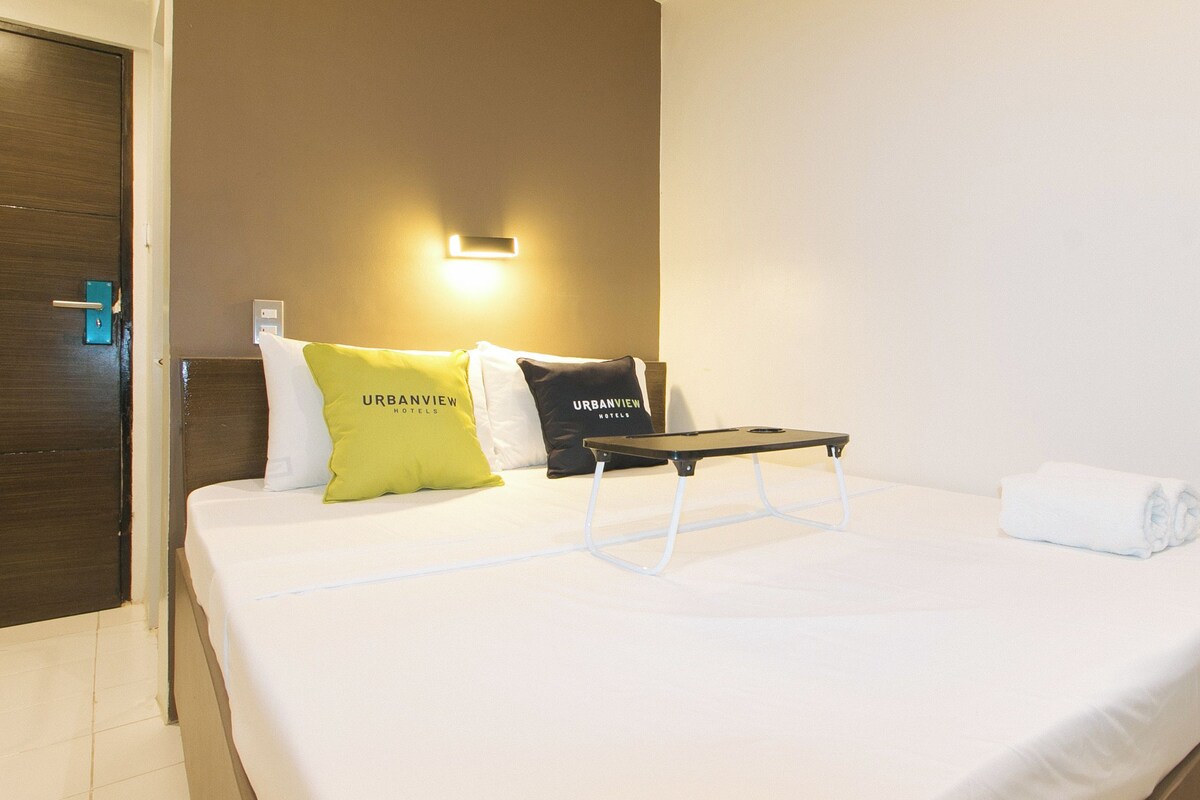 Ein Hotelzimmer mit Bett, Nachttisch, Wandlampe und einer Zimmerpflanze.