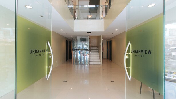 A modern hotel lobby with glass walls, a staircase, and a view of the street. - UrbanViewSanAntonio'sPlaceSampalocManila (Manila)