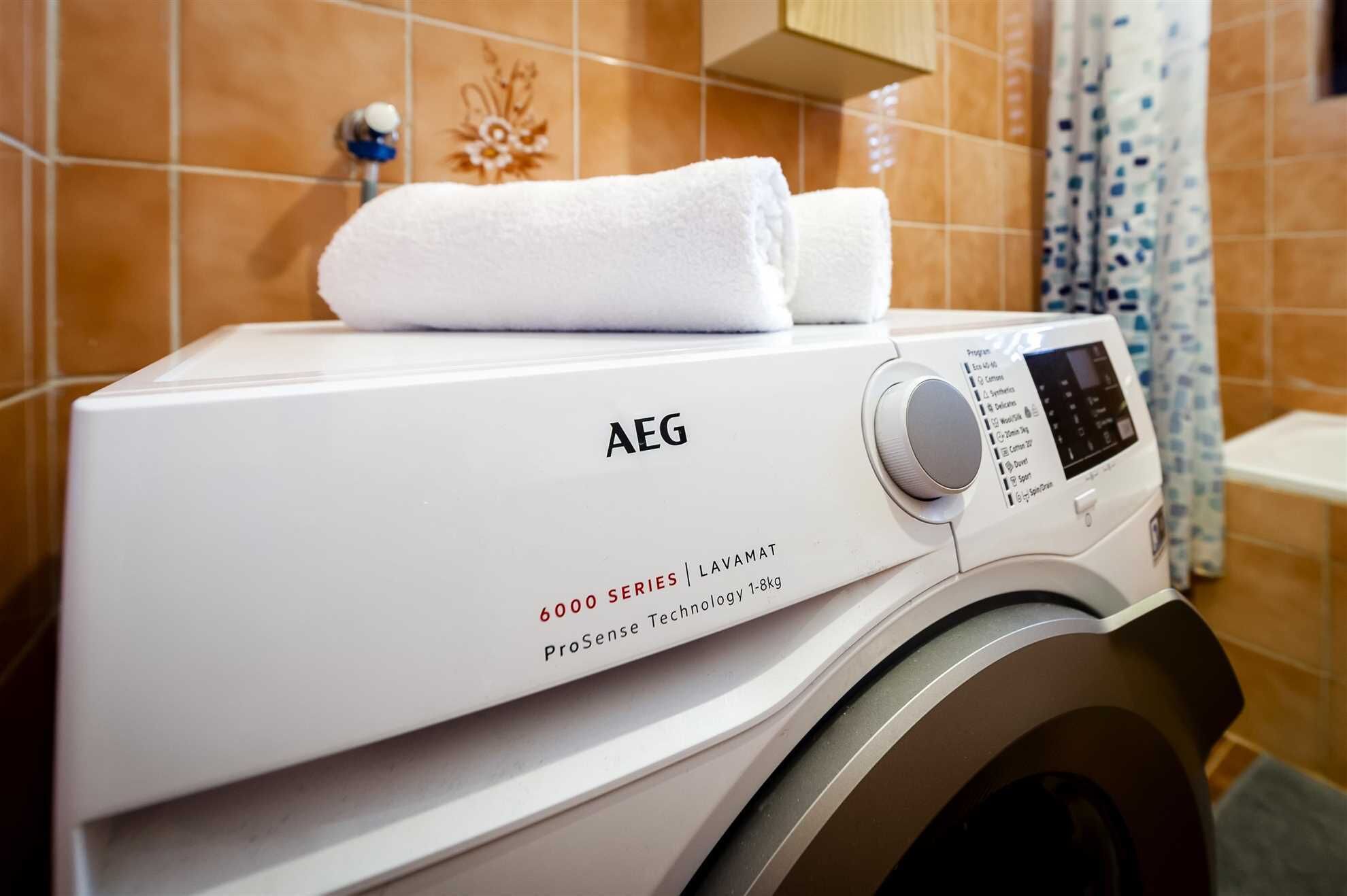 A front view of a white AEG washing machine with a control panel and a folded white towel on top.