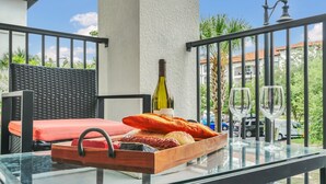 A balcony with a glass table, a bottle of wine, two glasses, and a wooden tray with bread and cheese. - Stylish and New! 3br, Steps fr. Universal Drive (Orlando)