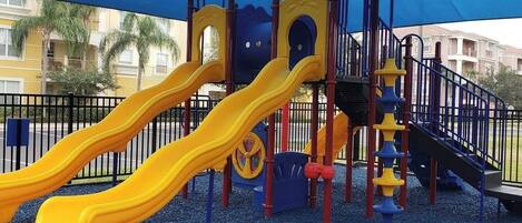 A playground with two yellow slides, a climbing structure, and a covered area.