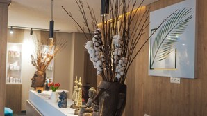 Un mostrador de recepción con jarrones decorativos, incluyendo uno con ramas de algodón, y una obra de arte con hojas enmarcada en la pared.