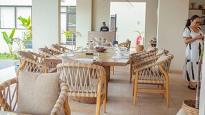Un comedor con sillas de mimbre, una mesa de madera y un mostrador de recepción al fondo.