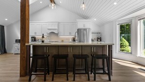 Una cucina moderna con una grande isola, sgabelli di legno scuro, mobili bianchi e vista sul verde circostante.