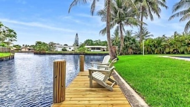 A wooden dock leading to a pool with a chair, surrounded by palm trees and a clear sky. - Tranquil Waterside Retreat (Oakland Park)