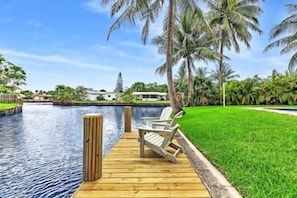 A wooden dock leading to a pool with a chair, surrounded by palm trees and a clear sky. - Tranquil Waterside Retreat (Oakland Park)