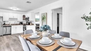 A modern kitchen with white cabinets, a dining table set with white plates and bowls, and a gray sofa. - Tranquil Waterside Retreat (Oakland Park)