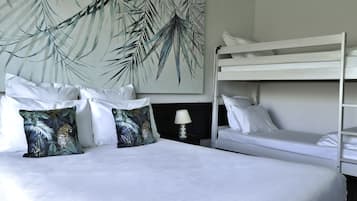 Habitación de hotel con una cama litera, una cama grande con ropa de cama blanca y una pared con diseño de hojas tropicales.