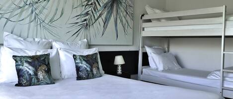 A hotel room with a bunk bed, a large bed with white bedding, and a wall with a tropical leaf pattern.