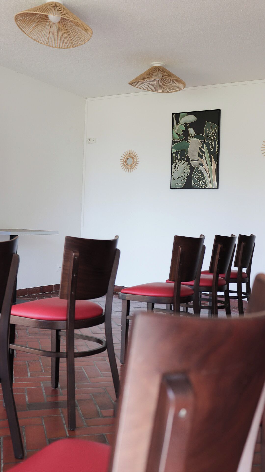 A dining area with wooden chairs and a table, a wall-mounted artwork, and two ceiling lamps.
