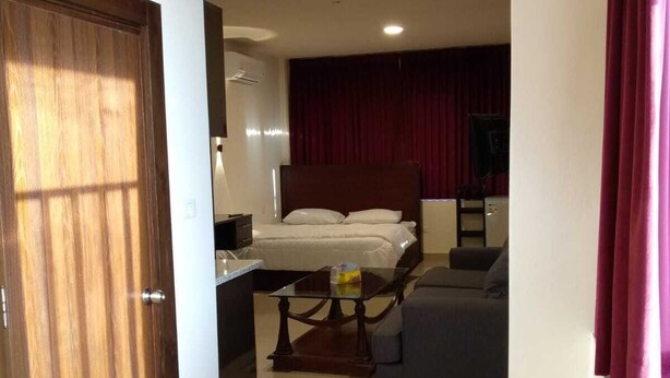 A hotel room with a bed, a sofa, a small table, and a TV. - Monument Suites  (Amman)