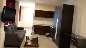 A compact living space with a sofa, a coffee table, a flat-screen TV mounted on the wall, a kitchenette with cabinets, and a wardrobe. - Monument Suites  (Amman)