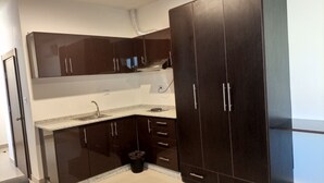 A compact kitchen with dark cabinets, a granite countertop, and a small trash bin. - Monument Suites  (Amman)