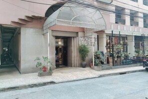L’entrée d’un hôtel, dotée d’un auvent, agrémentée de plantes en pot et d’une enseigne bien visible.