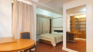 A hotel room with a bed, a wooden table, a chair, a mirror, and a closet with shelves. - Sunette Tower Makati (Makati)