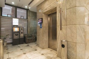 An elevator area with a marble wall, a trash bin, and a payment machine. - Sunette Tower Makati (Makati)