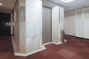 Un couloir avec un pilier de marbre, un ascenseur et une poubelle.