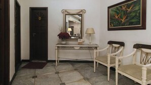 A hallway with a door, a mirror, a table with a lamp, and two chairs. - Sunette Tower Makati (Makati)