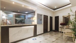 A reception area with a marble floor, a reception desk, a wall-mounted TV, and a door leading to another room. - Sunette Tower Makati (Makati)