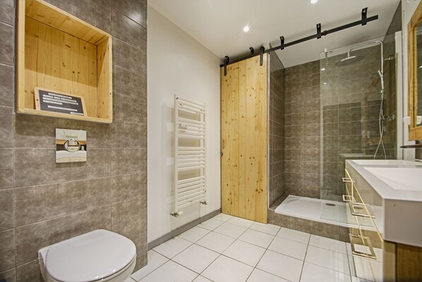 A bathroom with a toilet, a wooden cabinet, a shower with a glass door, and a white tiled floor.