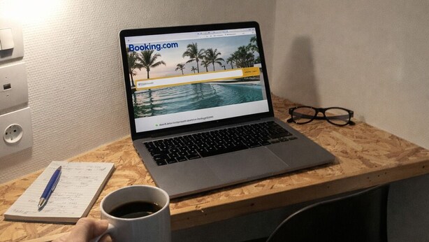 Una computadora portátil sobre un escritorio con una página web abierta, una taza de café, un bolígrafo, gafas y una lámpara.