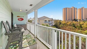 A balcony with a view of tall buildings, a lifeguard sign, and a wooden chair. - Dog Friendly Getaway Steps to Beach & Pool, Coffee Bar, K Bed, Putting Green (Panama City Beach)