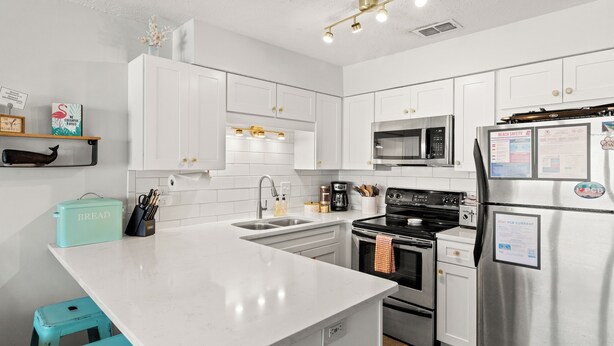 A modern kitchen with white cabinetry, stainless steel appliances, and a central island. - Dog Friendly Getaway Steps to Beach & Pool, Coffee Bar, K Bed, Putting Green (Panama City Beach)
