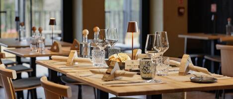 Een restaurant met houten tafels en stoelen, helder glaswerk en een menubord.