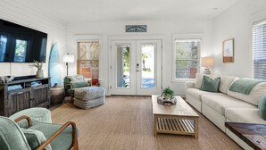 A living room with a sofa, armchair, coffee table, TV, and a view through the door. - Family & Pet-Friendly 30A Villa – Private Pool w/Heat, 3BR, 5 Bikes, Near Beach (Santa Rosa Beach)