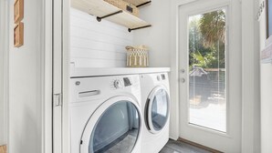 A laundry room with two front-loading washing machines, wooden shelves with baskets, and a door with a window. - Family & Pet-Friendly 30A Villa – Private Pool w/Heat, 3BR, 5 Bikes, Near Beach (Santa Rosa Beach)
