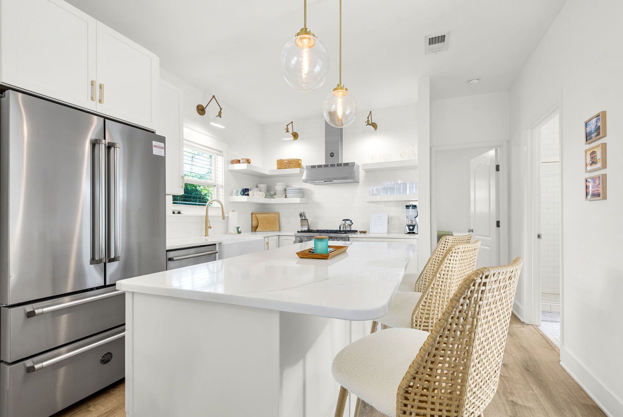 A modern kitchen with white cabinetry, stainless steel appliances, and a central island with wicker chairs.