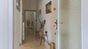 En hall med ett element, ett litet bord med dekorativa föremål och en dörr med en mönstrad gardin.