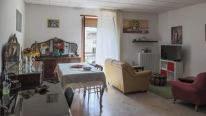 Ett vardagsrum med ett matbord, en soffa och en röd fåtölj. Det finns en tv och ett element på väggen.