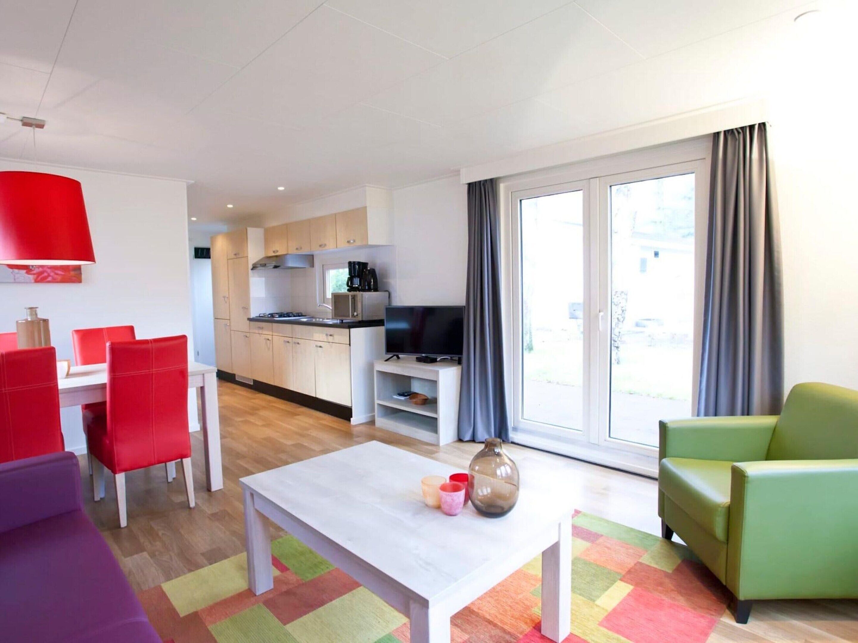Een moderne woonkamer met een eetgedeelte, een keuken en een grote schuifpui naar buiten.
