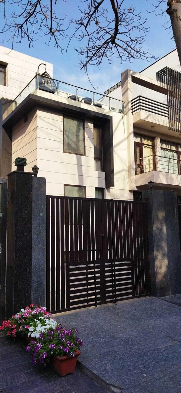A modern building with a gated entrance, potted plants, and a clear sky. - TAVISHA VILLA FILM CITY ROAD (Noida)