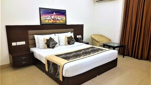 A hotel room with a large bed, a bedside table, a chair, a TV mounted on the wall, and an air conditioning unit.
