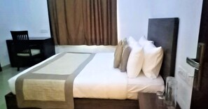A neatly made bed with a beige and white duvet, a dark headboard, and several pillows. There is a chair and a small table with a glass on it in the room. - TAVISHA VILLA FILM CITY ROAD (Noida)