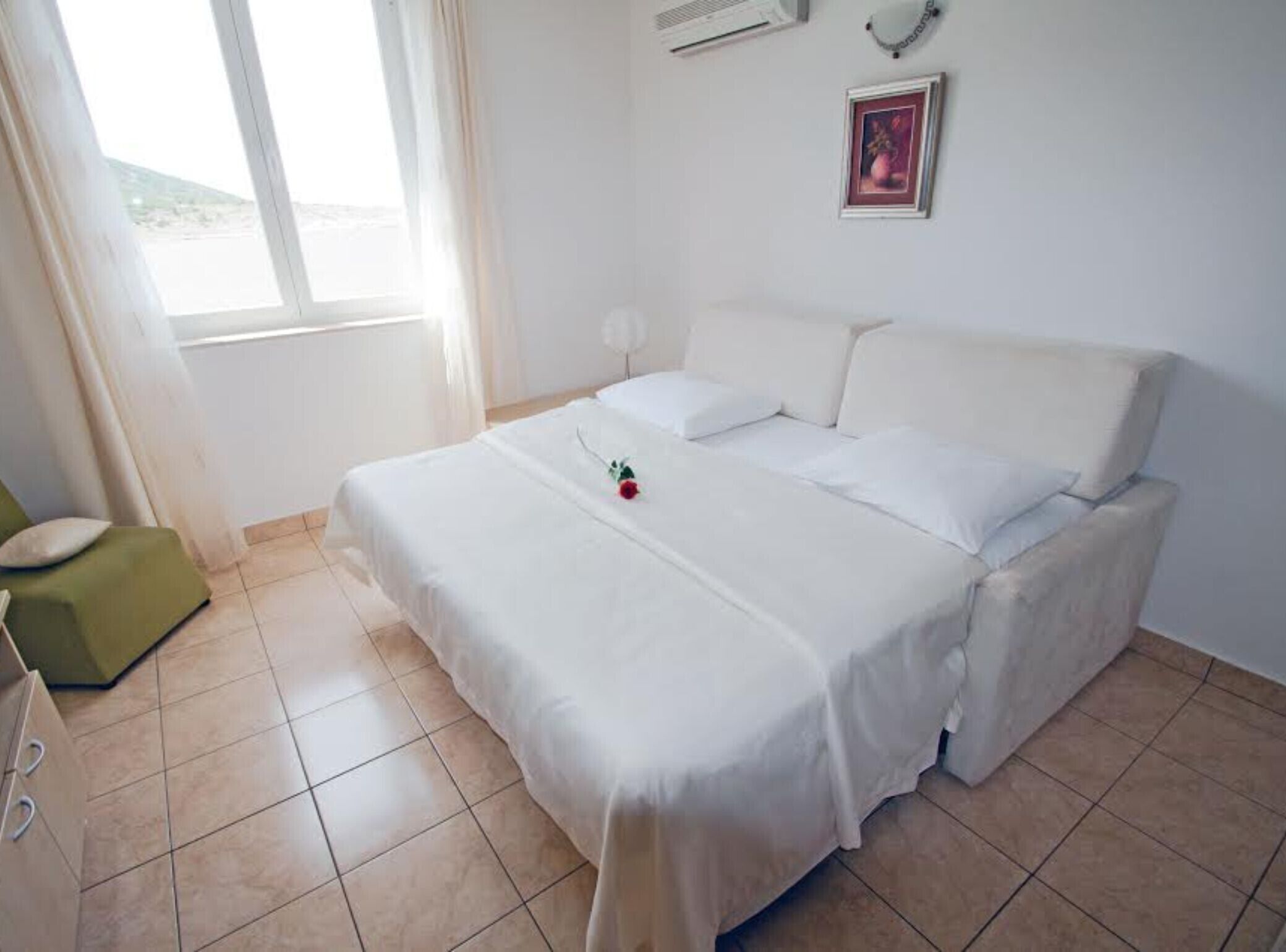 A bedroom with a bed, a green chair, a window, and a picture on the wall.
