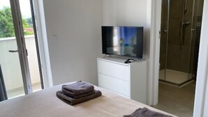 Ein Schlafzimmer mit einem Bett, einem Fernseher auf einem Schrank, einer weißen Kommode und einer Duschkabine.