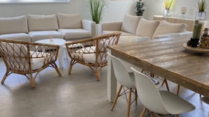 Ein modernes Wohnzimmer mit einem beigefarbenen Sofa, Korbstühlen, einem Holzesstisch und weißen Stühlen.